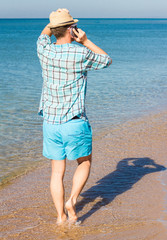 Hipster with hat talking on phone against the sea. Summer holiday