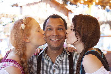 Young man getting kissed on the cheek by two german girls at Oktoberfest