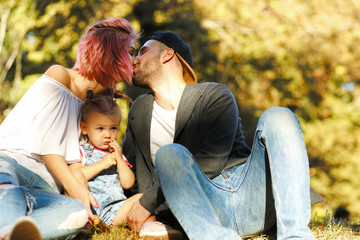 Stylish young parents kiss over their lovely little daughter