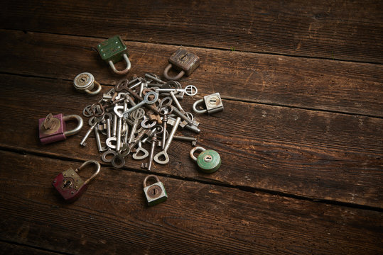 Group of old rusty padlocks with pile of keys on brown wooden table
