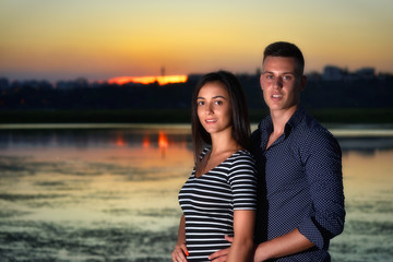 Young couple in love against a lake with reflections at sunset