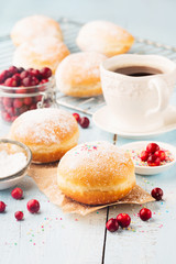 Delicious freshly baked doughnuts with powdered sugar and cup of coffee on blue rustic wooden background.