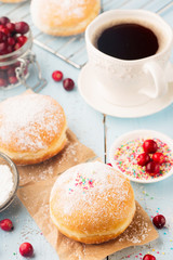 Delicious freshly baked doughnuts with powdered sugar and cup of coffee on blue rustic wooden table. Breakfast concept, Selective focus.