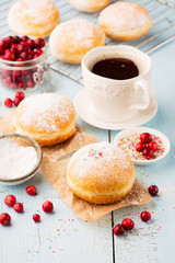 Delicious freshly baked doughnuts with powdered sugar and cup of coffee on blue rustic wooden background. Breakfast concept, Selective focus.