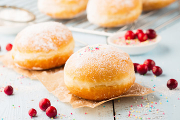 Delicious freshly baked doughnuts with powdered sugar and fruit jam on blue wooden background. Selective focus.