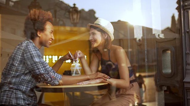 Two beautiful girls smiling speaking holding hands resting in cafe Slow motion