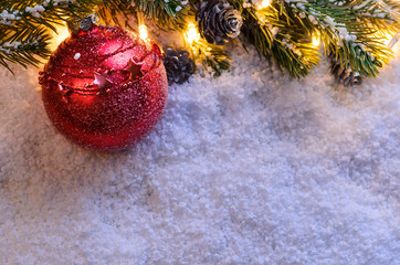 Christmas fir tree with lights and toy ball on snow in dark, view from above