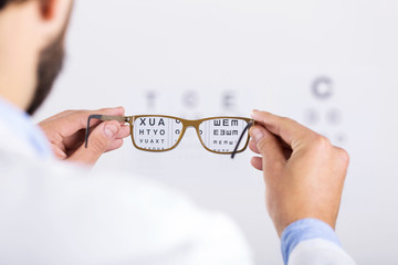 optician holds glasses in front of eyesight test chart