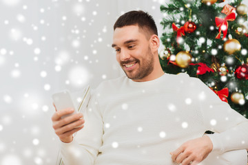 smiling man with smartphone at home for christmas