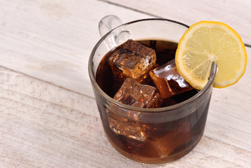 Cola drink with ice cube and lemon slice on white rustic wood background