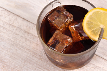 Cola drink with ice cube and lemon slice on white rustic wood background top view