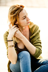 Blonde woman sits on the road holding her hair together