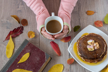 Female hands holding cup of coffee on wooden background. Autumn