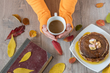 Female hands holding cup of coffee on wooden background. Autumn