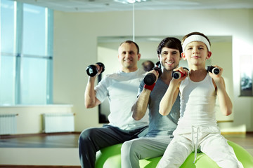 Three different males exercising with dumbbells in gym 