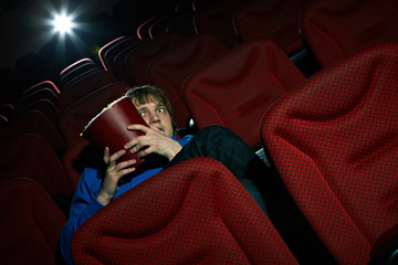 Naklejka premium Young man sitting terrified in cinema hall