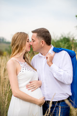 Portrait happy and young pregnant couple hugging in nature