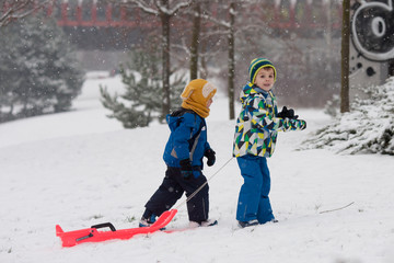 Two kids, boy brothers, sliding with bob in the snow, wintertime