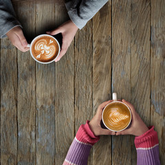 Female hands holding cups of latte art coffee on rustic wooden table background