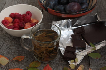 on the dark wooden table hot green tea, chocolate, apples, plums, raspberry, book. cozy autumn or winter evening.
