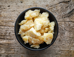 Pieces of parmesan cheese in black bowl on wooden table, from ab