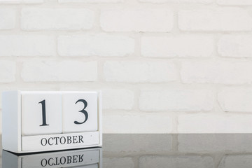 Obraz premium Closeup white wooden calendar with black 13 october word on black glass table and white brick wall textured background with copy space , view another more date in my portfolio