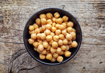 Black bowl of chickpeas on wooden table, from above