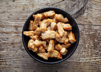 Black bowl of grilled pork chunks on wooden table, from above