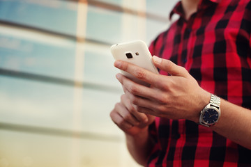 Cropped shot view of man`s hands holding smart phone. Yong man using mobile phone. Glass wall with...