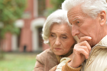 Sad elderly couple standing embracing outdoors