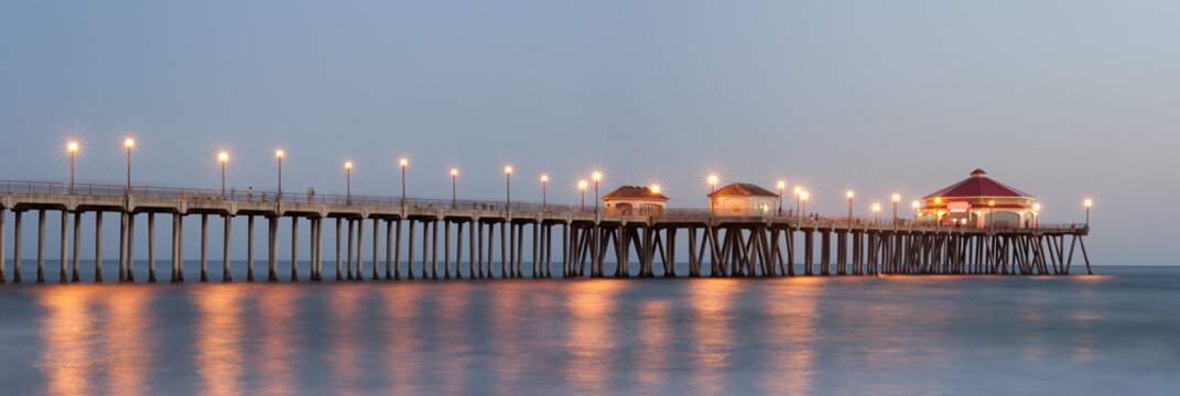 Fototapeta Panorama of Huntington beach pier lit up by street lights at dusk 