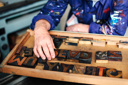 Senior craftsman reaching for wooden letterpress letters, mid section