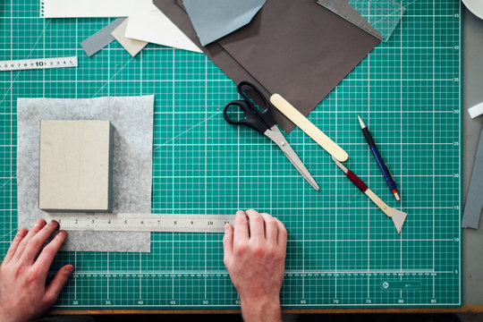 Overhead detail of hands, paper, cutting mat, ruler, scalpel and scissors in print studio