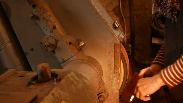 The blacksmith sharpening an ax on electrical grinder