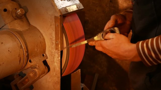 The blacksmith sharpening an ax on electrical grinder