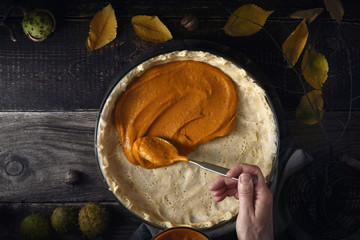 Putting  pumpkin puree on the dough for pumpkin pie on the wooden table