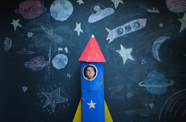 Portrait of girl in handmade space rocket in front of space themed chalk drawings