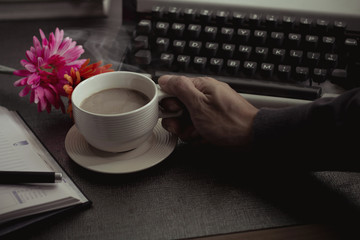 Vintage typewriter and coffee on stone board. Hand holder coffee cup.