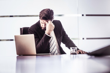 Stressed businessman with hand on forehead at office desk