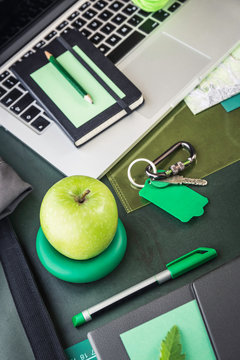 Laptop, notebook, folding map and green apple on table