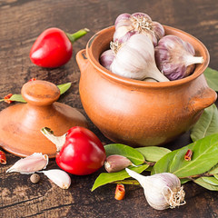 Spices.   Clay pot with heads of garlic, pods of red bitter pepper and fresh bay leaves on a brown...