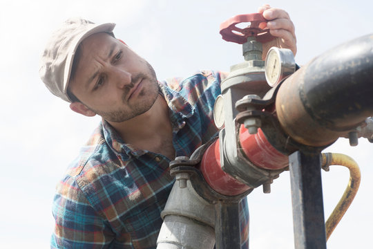 Man opening valve on industrial piping