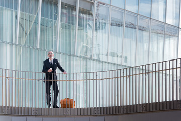 Middle-age contemporary businessman leaning on a handrail holding smart phone - work, business, technology concept