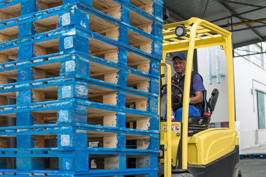 Forklift driver loading stacked pallets at packaging factory