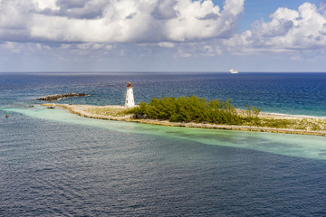 Lighthouse on peninsula in deep blue ocean under beautiful fluffy clouds in background