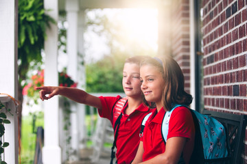 Twin brother and sister sitting on bench pointing, on first day of new school year