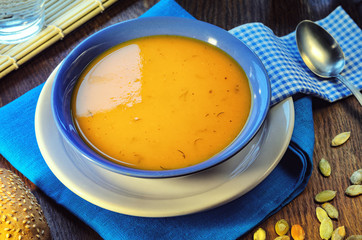 Pumpkin cream-soup. Hot pumpkin soup with toasted sesame seeds in a blue bowl on a wooden table. Still life with a bowl of soup, spoon, pumpkin seeds and slice of baguette