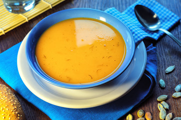 Pumpkin cream-soup. Hot pumpkin soup with toasted sesame seeds in a blue bowl on a wooden table. Still life with a bowl of soup, spoon, pumpkin seeds and slice of baguette