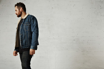Beautiful bearded man weared shearling denim jacket and black blank clothes isolated on white brick wall in club
