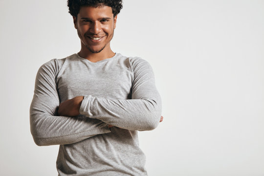 Jouyful smiling young attractive latino guy in blank grey longsleeve looks at camera and folds hands on his chest